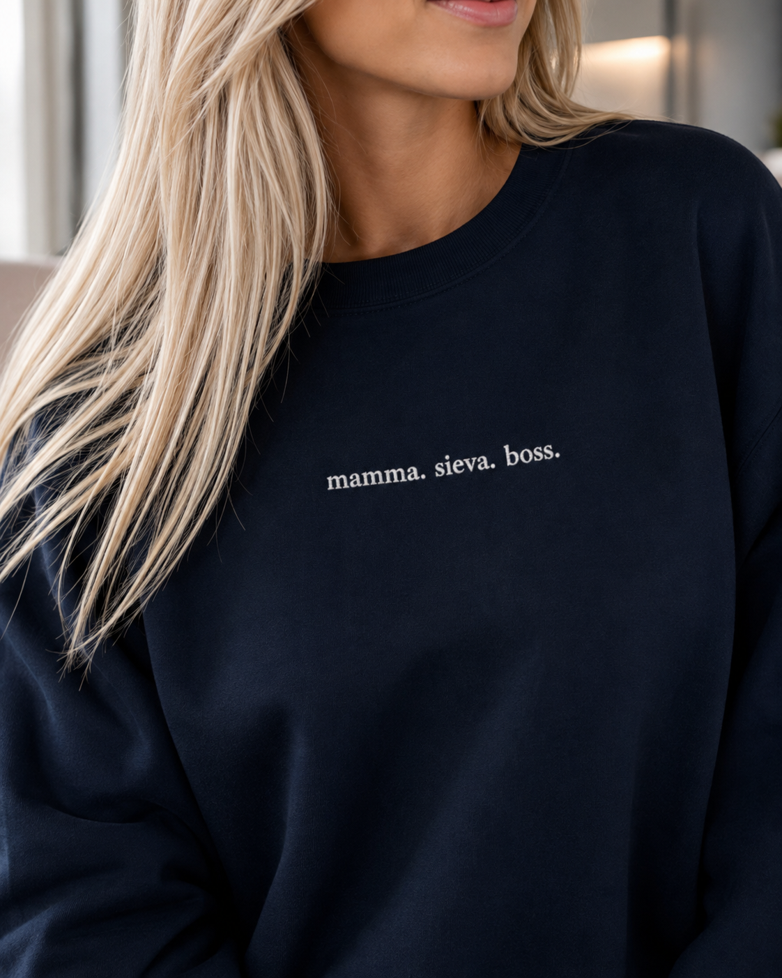 A close-up of a woman wearing a dark navy crewneck sweatshirt with the text 'mamma. sieva. boss"